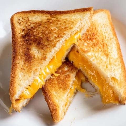 Two buttery Grilled Cheese Sandwich halves sit on a cutting board, perfect for pairing with a warm bowl of tomato soup. 