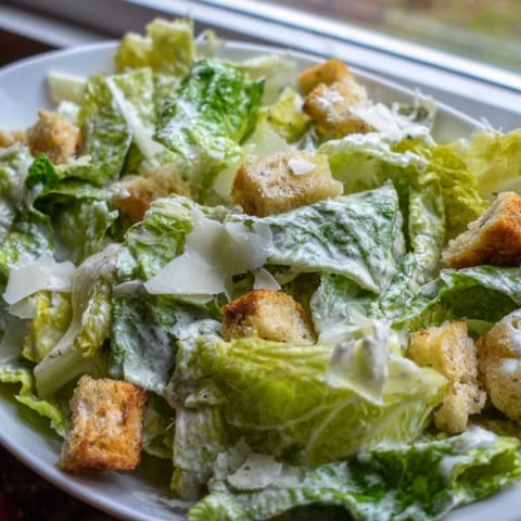 Vibrant green Caesar Salad topped with extra Parmesan shavings and golden-brown croutons, ready to be served as a delicious side dish at dinner.