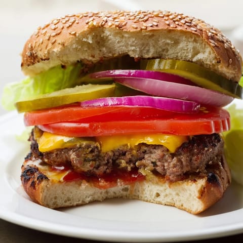 Grilled classic American hamburgers topped with crisp lettuce, ripe tomato, and onions on a soft sesame bun.