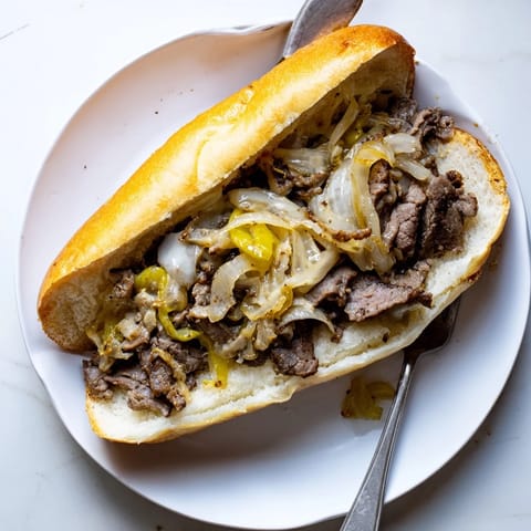 A close-up of a classic Philly Cheesesteak sandwich, overflowing with juicy beef and caramelized onions on a soft roll.