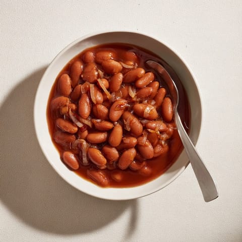 Golden-brown Baked Beans bubbling in a Dutch oven, featuring smoky aromas and tender navy beans swimming in a thick molasses glaze.