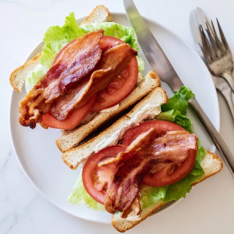 Golden toasted bread layered with crispy bacon, fresh lettuce, juicy tomato slices, and creamy mayonnaise, showing a classic BLT Sandwich cut in half on a plate.