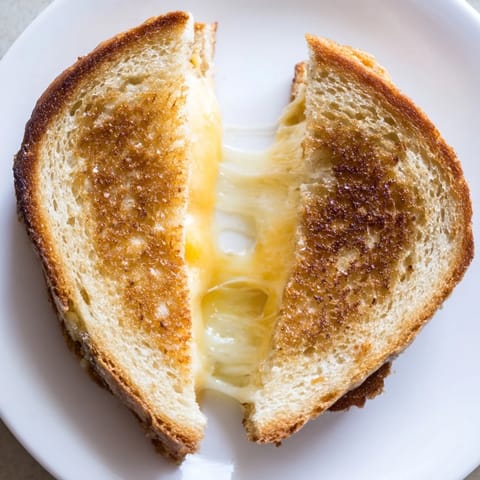 A close-up of a gooey Three-Cheese Grilled Cheese on sourdough, served beside a warm bowl of tomato soup.  