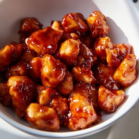 A close-up of a vibrant sweet chili chicken bowl, garnished with sesame seeds and sliced green onions on a rustic kitchen table.  