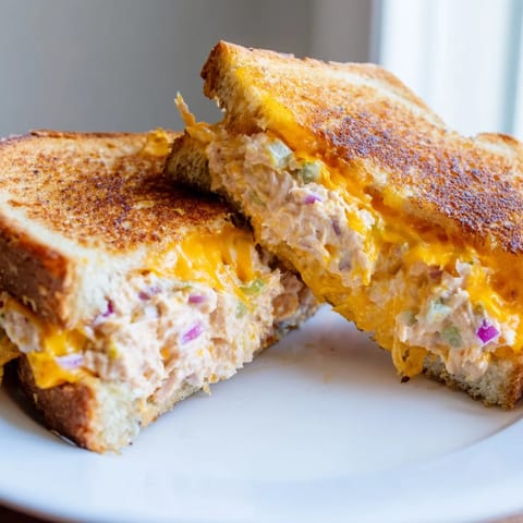 Close-up of a spicy tuna melt on toasted sourdough with fresh celery, red onion, and melted cheese oozing.
