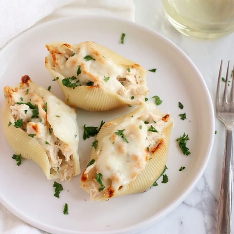 A close view of creamy Chicken Alfredo Stuffed Shells filled with chicken and ricotta, steaming beside a fork and salad.
