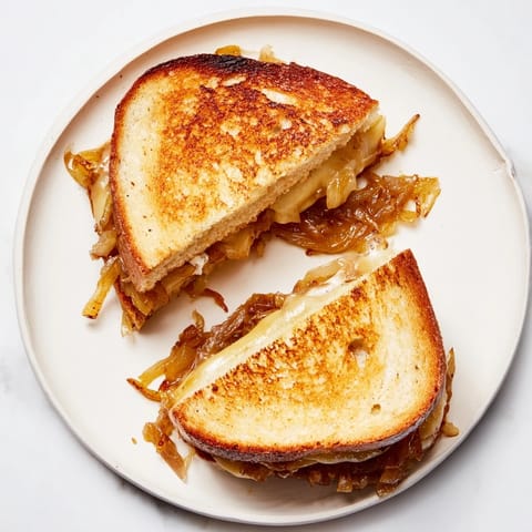 Close-up view of a Caramelized Onion & Gruyère Grilled Cheese sandwich, buttery and golden brown.  