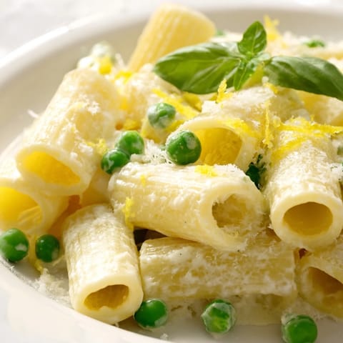 A close-up of a spring-inspired Pea & Lemon Ricotta Pasta serving, highlighting the silky lemon sauce and extra grated Parmesan on top.