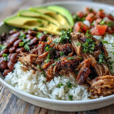 A top-down view of a hearty Carnitas Bowl with slow-cooked pork over fluffy rice, topped with pinto beans, fresh salsa, and sliced avocado.