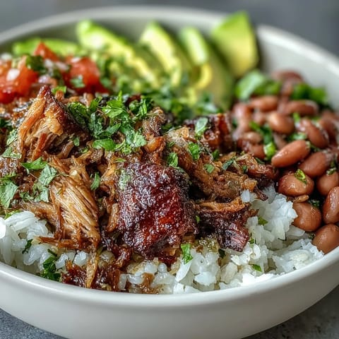 A close-up of a Carnitas Bowl featuring tender, crispy-edged pork, creamy avocado slices, and vibrant salsa, served with a lime wedge on the side.