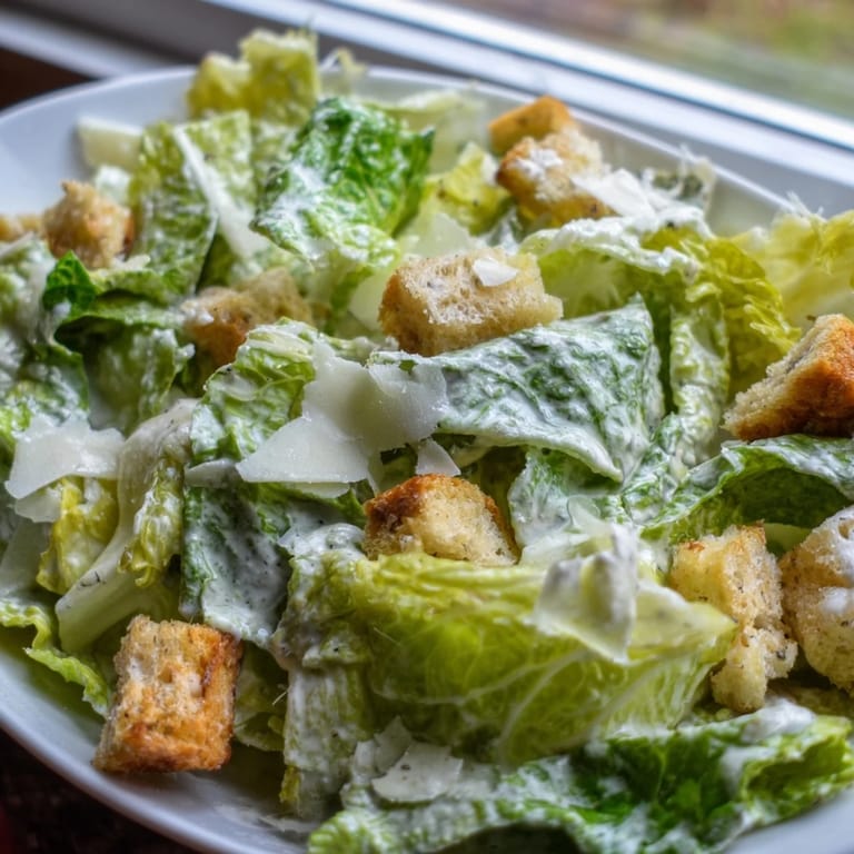 Vibrant green Caesar Salad topped with extra Parmesan shavings and golden-brown croutons, ready to be served as a delicious side dish at dinner.