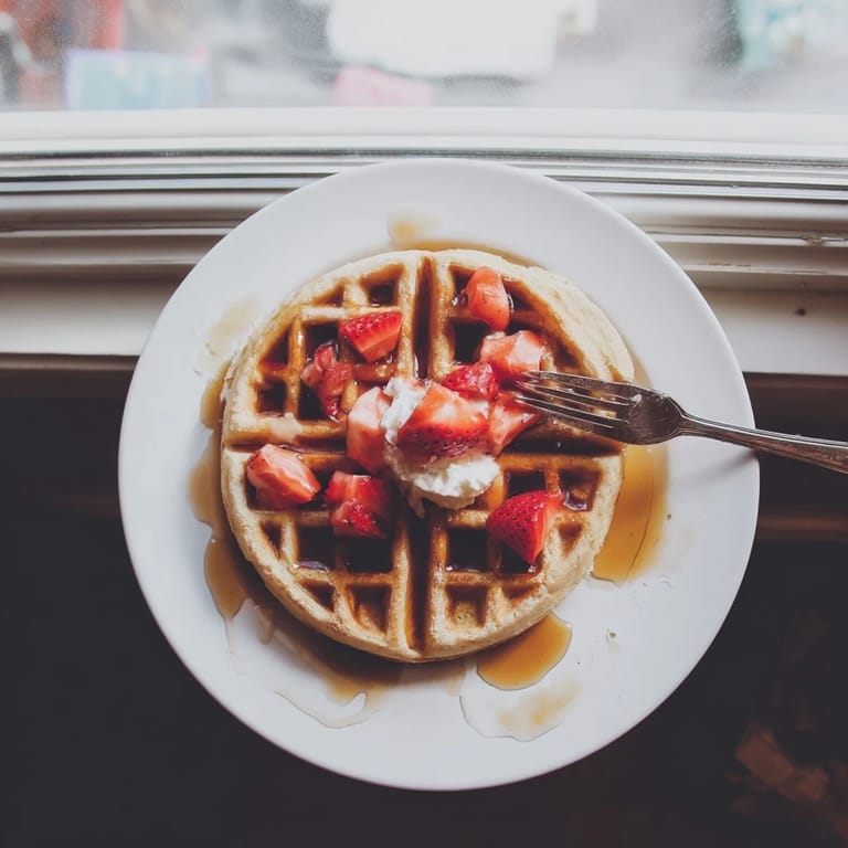 Steam rises from the crispy, fluffy waffles served with whipped cream and fresh fruit for a sweet breakfast. 