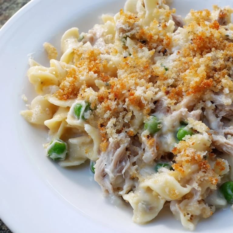 Bubbling cheesy tuna casserole with flaky tuna, sweet peas, and golden breadcrumbs in baking dish.