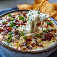 Creamy Queso Dip in a bowl, topped with cilantro and diced tomatoes, with tortilla chips on the side.