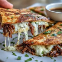A golden quesadilla stuffed with juicy birria beef, served with a steaming cup of spicy consommé for dipping.